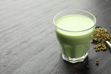 Photo of Fresh mung bean juice in glass and seeds on black table, closeup. Space for text