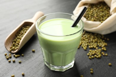 Photo of Fresh mung bean juice in glass, seeds and scoop on black table, closeup