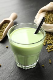 Photo of Fresh mung bean juice in glass, seeds and scoop on black table, closeup