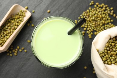 Photo of Fresh mung bean juice in glass, seeds and scoop on black table, flat lay