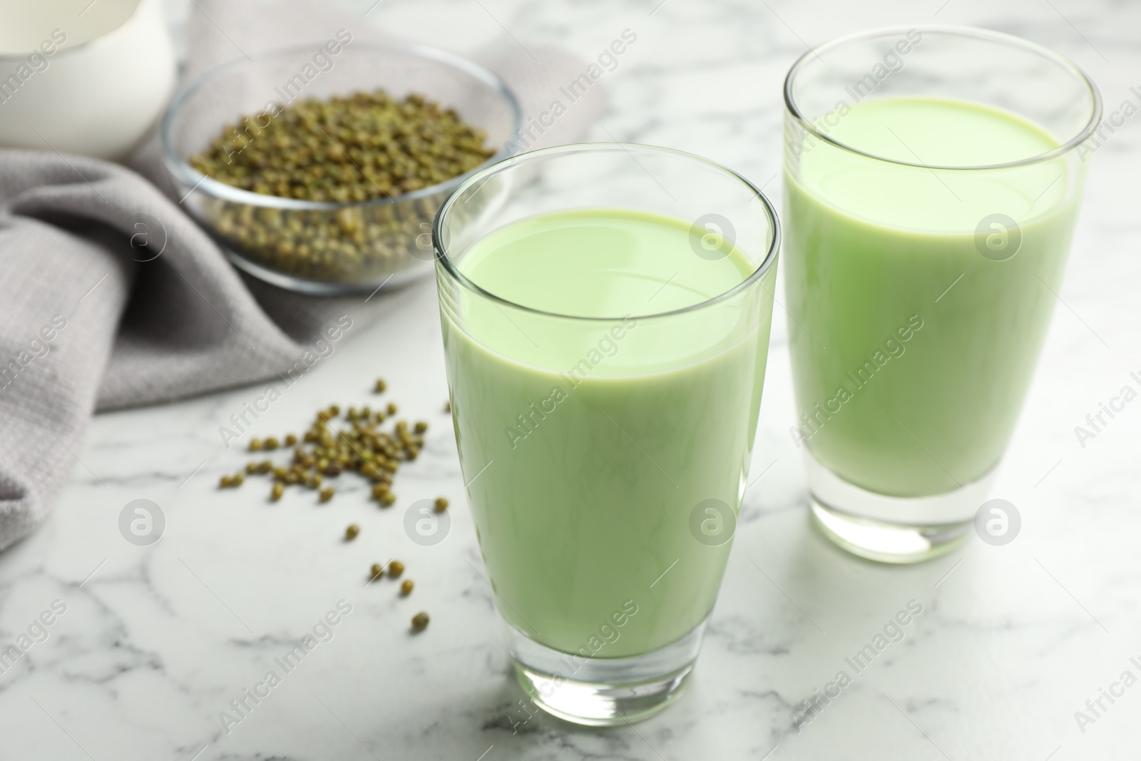 Fresh mung bean juice in glasses and seeds on white marble table, closeup Photo of Fresh mung bean juice in glasses and seeds on white marble table, closeup