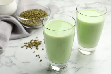 Photo of Fresh mung bean juice in glasses and seeds on white marble table, closeup