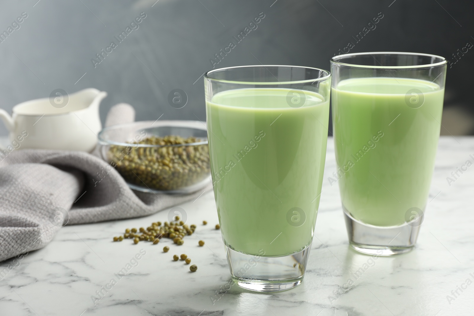 Fresh mung bean juice in glasses and seeds on white marble table Photo of Fresh mung bean juice in glasses and seeds on white marble table