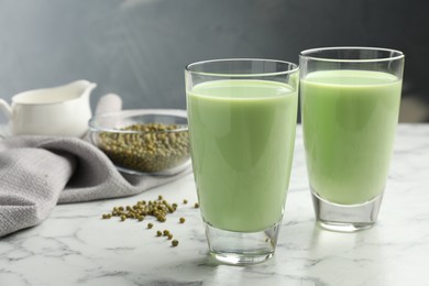 Photo of Fresh mung bean juice in glasses and seeds on white marble table