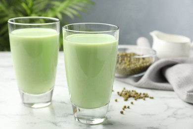 Photo of Fresh mung bean juice in glasses and seeds on white marble table, closeup