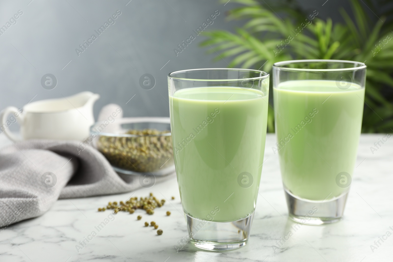 Fresh mung bean juice in glasses and seeds on white marble table Photo of Fresh mung bean juice in glasses and seeds on white marble table