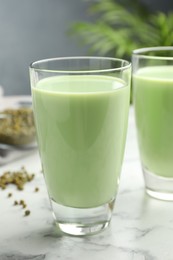 Photo of Fresh mung bean juice in glasses and seeds on white marble table, closeup