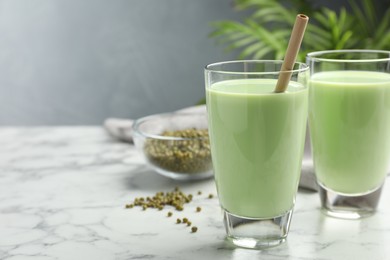 Photo of Fresh mung bean juice in glasses and seeds on white marble table, closeup. Space for text