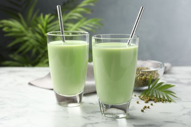 Photo of Fresh mung bean juice in glasses, seeds and twig on white marble table