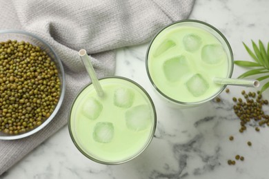Photo of Fresh mung bean juice in glasses, seeds and green twig on white marble table, flat lay