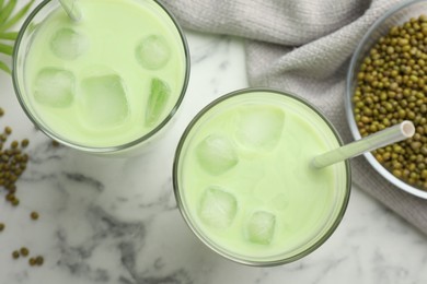 Photo of Fresh mung bean juice in glasses and seeds on white marble table, flat lay