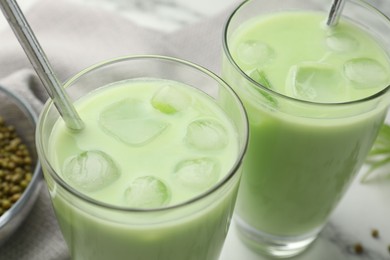 Photo of Fresh mung bean juice in glasses and seeds on table, closeup