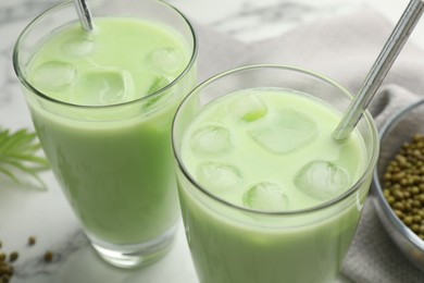 Photo of Fresh mung bean juice in glasses and seeds on white marble table, closeup