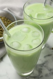 Photo of Fresh mung bean juice in glasses and seeds on white marble table, closeup