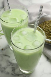 Photo of Fresh mung bean juice in glasses and seeds on white marble table, closeup