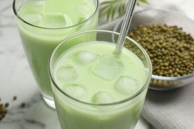 Photo of Fresh mung bean juice in glasses and seeds on white marble table, closeup