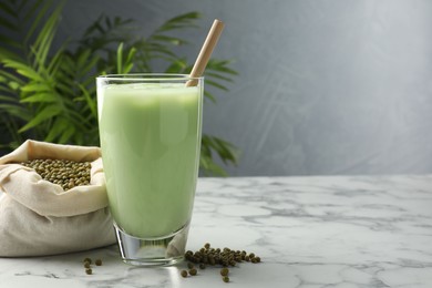 Photo of Fresh mung bean juice in glasses, seeds and green plant on white marble table, space for text