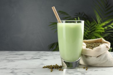 Photo of Fresh mung bean juice in glasses, seeds and green plant on white marble table, space for text