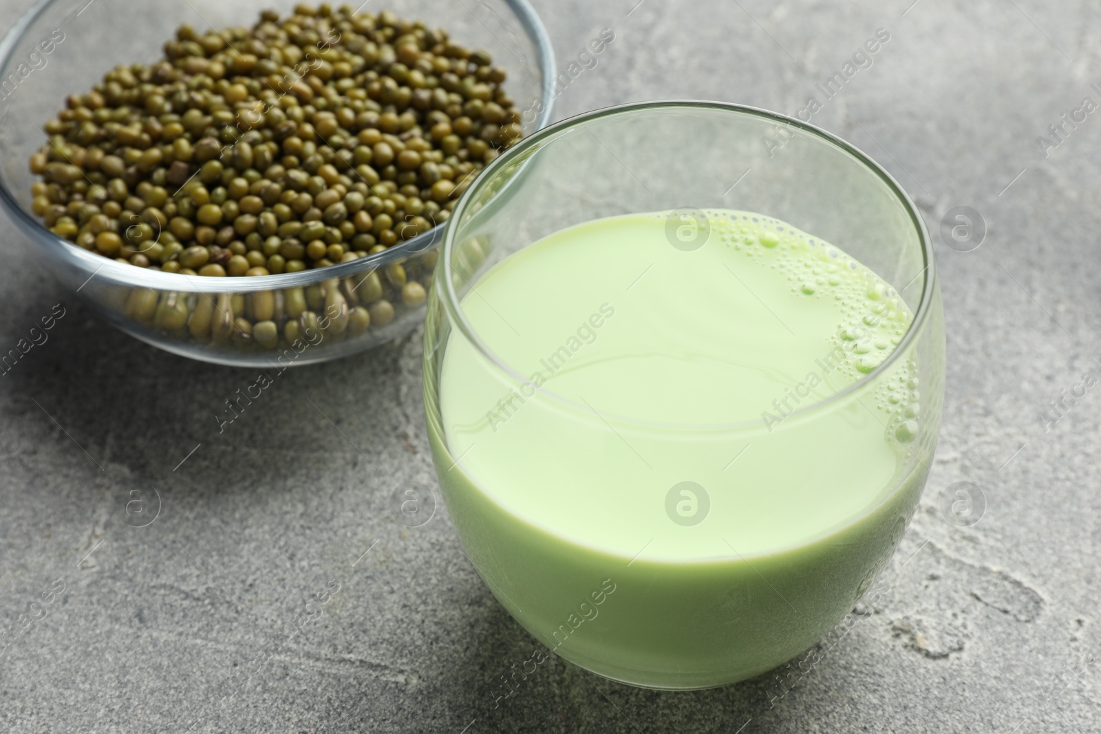 Fresh mung bean juice in glass and seeds on grey table, closeup Photo of Fresh mung bean juice in glass and seeds on grey table, closeup