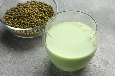 Photo of Fresh mung bean juice in glass and seeds on grey table, closeup