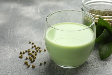 Photo of Fresh mung bean juice in glass, seeds and green leaves on grey table, closeup. Space for text