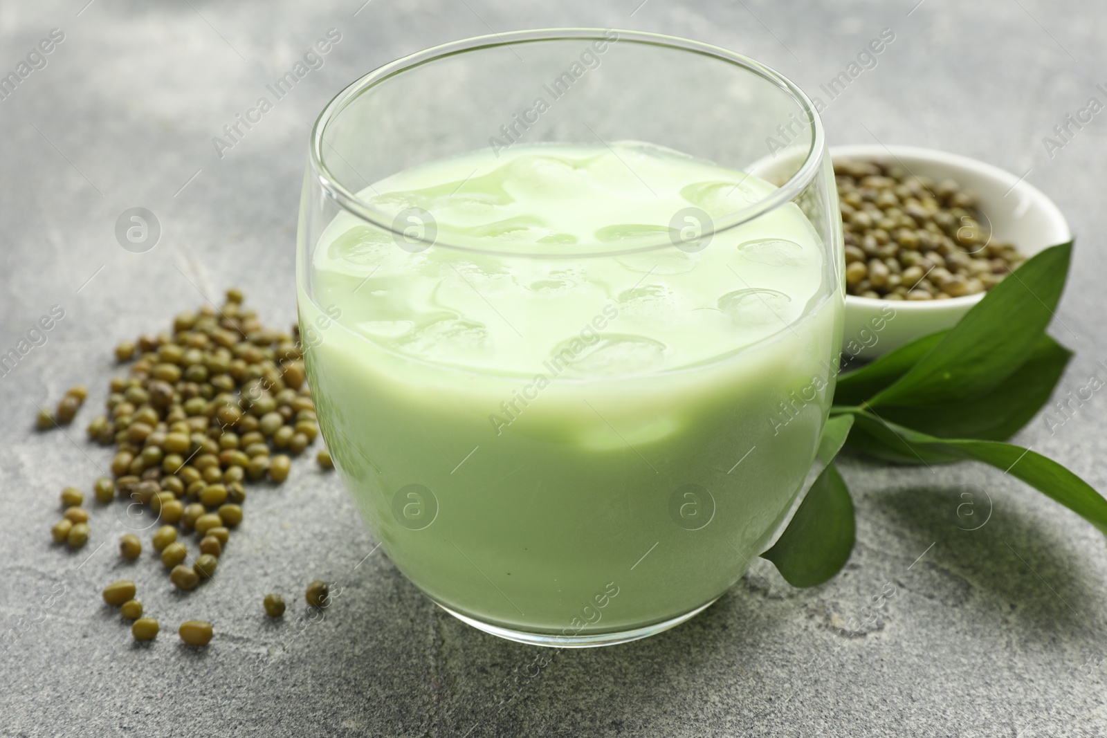Fresh mung bean juice in glass, seeds and green leaves on grey table, closeup Photo of Fresh mung bean juice in glass, seeds and green leaves on grey table, closeup
