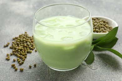 Photo of Fresh mung bean juice in glass, seeds and green leaves on grey table, closeup