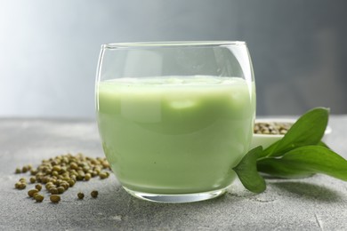 Photo of Fresh mung bean juice in glass, seeds and green leaves on grey table, closeup