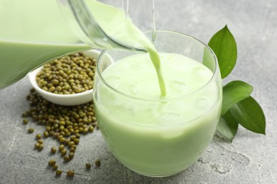 Photo of Pouring fresh mung bean juice in glass at grey table, closeup