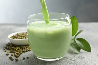 Photo of Pouring fresh mung bean juice in glass at grey table, closeup