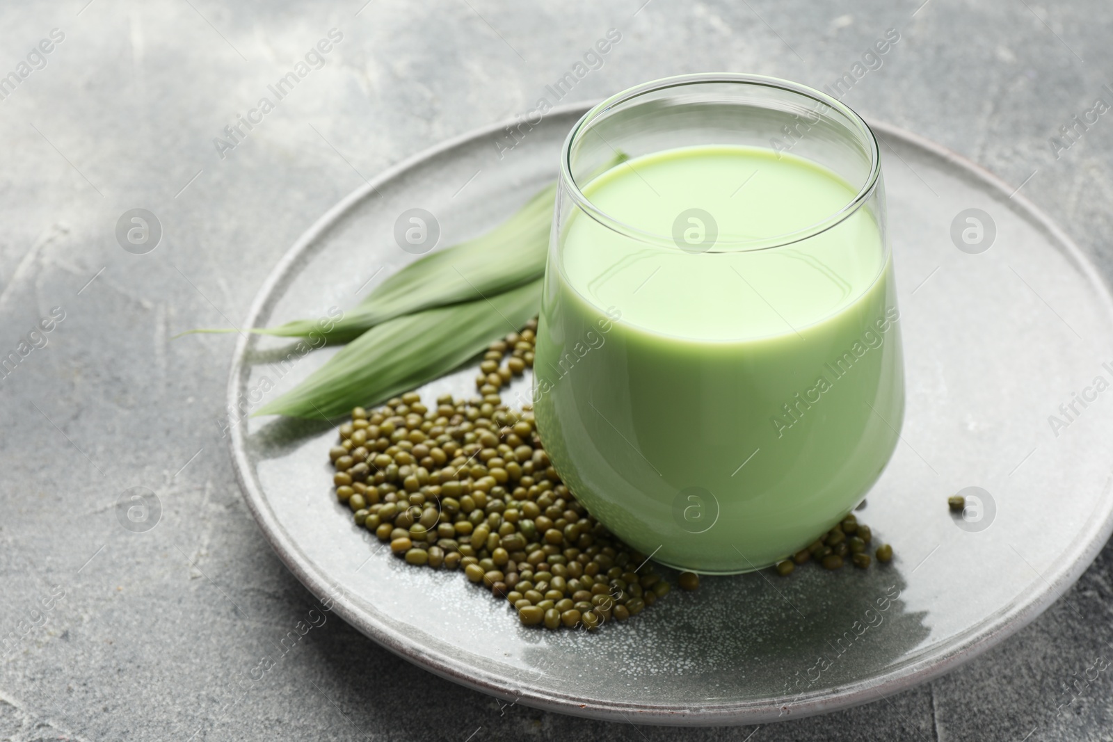 Fresh mung bean juice in glass, seeds and green leaves on grey table, closeup Photo of Fresh mung bean juice in glass, seeds and green leaves on grey table, closeup