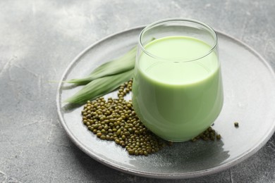 Photo of Fresh mung bean juice in glass, seeds and green leaves on grey table, closeup