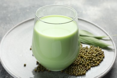 Photo of Fresh mung bean juice in glass, seeds and green leaves on table, closeup