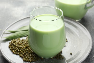 Photo of Fresh mung bean juice in glass, seeds and green leaves on table, closeup