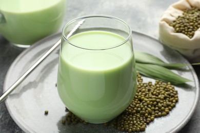 Photo of Fresh mung bean juice in glass, seeds and green leaves on table, closeup