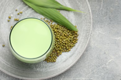 Photo of Fresh mung bean juice in glass, seeds and green leaves on grey table, top view