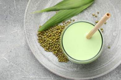 Photo of Fresh mung bean juice in glass, seeds and green leaves on grey table, top view