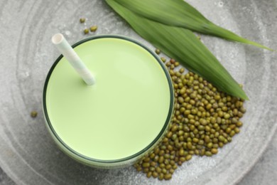 Photo of Fresh mung bean juice in glass, seeds and green leaves on table, top view