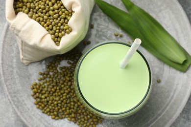 Photo of Fresh mung bean juice in glass, seeds and green leaves on table, top view