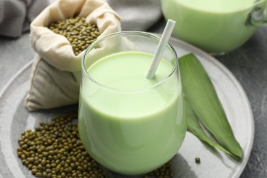 Photo of Fresh mung bean juice in glass, seeds and green leaves on table, closeup