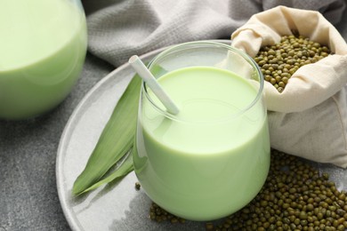 Photo of Fresh mung bean juice in glass, seeds and green leaves on grey table, closeup