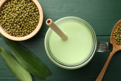 Photo of Fresh mung bean juice in mason jar, seeds and leaves on green wooden table, flat lay