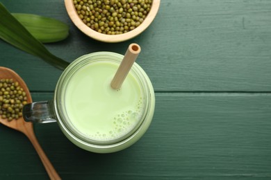 Photo of Fresh mung bean juice in mason jar, seeds and leaves on green wooden table, flat lay. Space for text