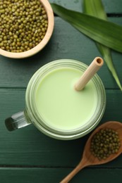 Photo of Fresh mung bean juice in mason jar, seeds and leaves on green wooden table, flat lay