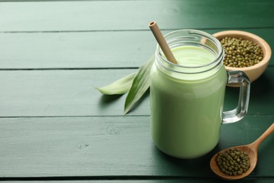 Photo of Fresh mung bean juice in mason jar, seeds and leaves on green wooden table, closeup. Space for text
