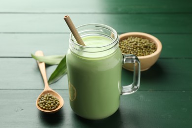 Photo of Fresh mung bean juice in mason jar, seeds and leaves on green wooden table, closeup
