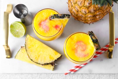 Photo of Tasty pineapple cocktail in glasses served on white table, flat lay