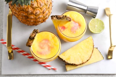 Photo of Tasty pineapple cocktail in glasses served on white table, flat lay