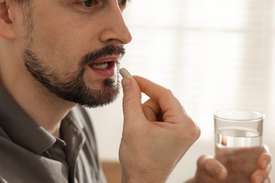 Photo of Man with glass of water taking pill at home, closeup