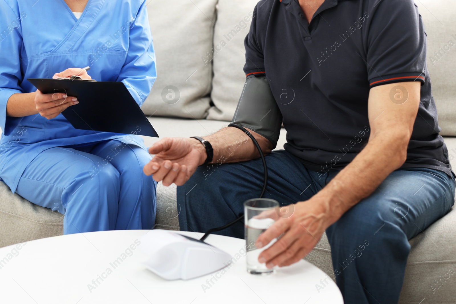 Photo of Nurse measuring senior man's blood pressure and writing results at home, closeup